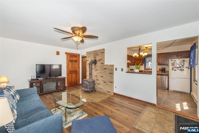 living area featuring wood finished floors, a wood stove, baseboards, and ceiling fan with notable chandelier