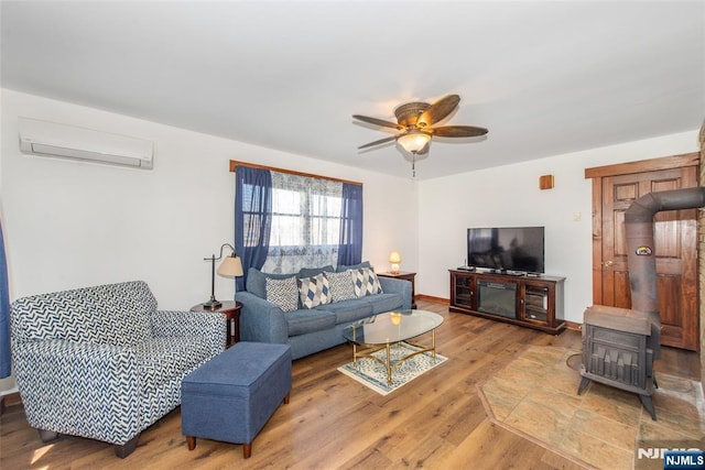 living room featuring baseboards, a ceiling fan, wood finished floors, a wall mounted AC, and a wood stove