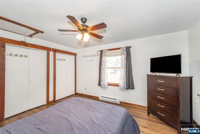 bedroom with baseboard heating, a ceiling fan, wood finished floors, multiple closets, and a wall mounted AC