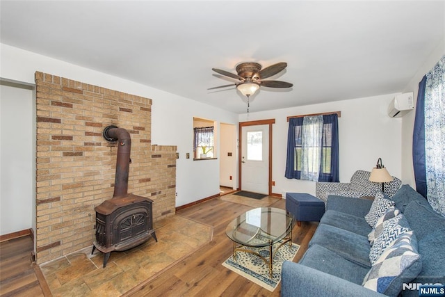 living room with baseboards, a wall mounted air conditioner, wood finished floors, ceiling fan, and a wood stove