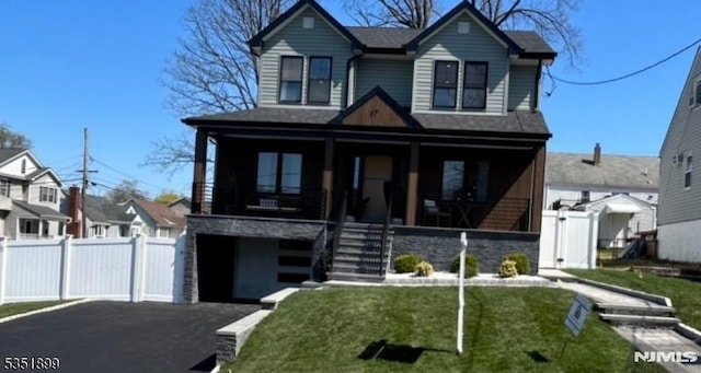traditional-style home featuring a gate, a front lawn, stone siding, fence, and a porch