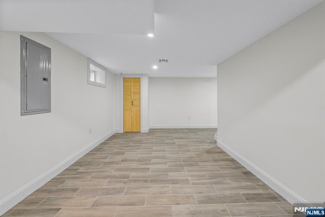 finished below grade area featuring electric panel, light wood-style flooring, baseboards, visible vents, and recessed lighting