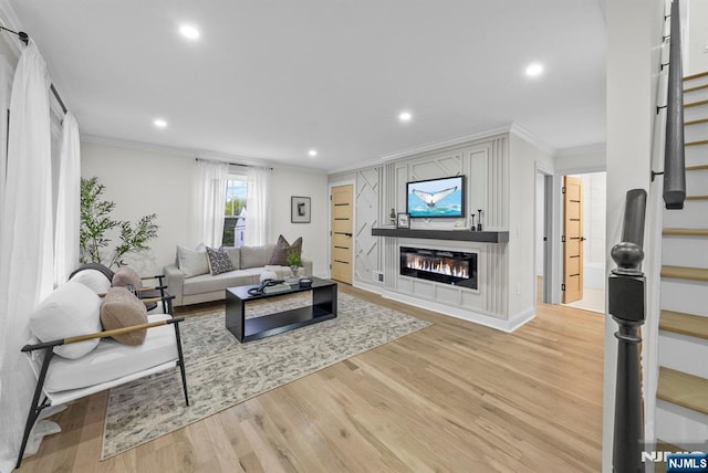 living room featuring light wood finished floors, a glass covered fireplace, stairs, and crown molding