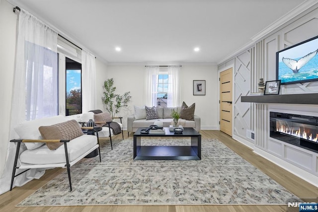 living area featuring ornamental molding, a glass covered fireplace, wood finished floors, and recessed lighting