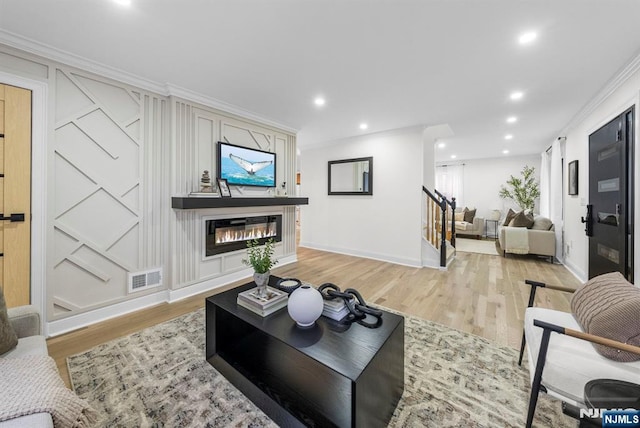 living room featuring crown molding, a glass covered fireplace, light wood-style flooring, baseboards, and visible vents