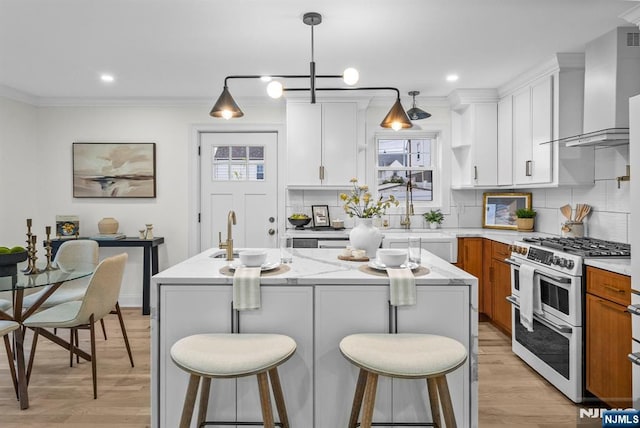 kitchen with range with two ovens, crown molding, light wood-style flooring, and wall chimney exhaust hood