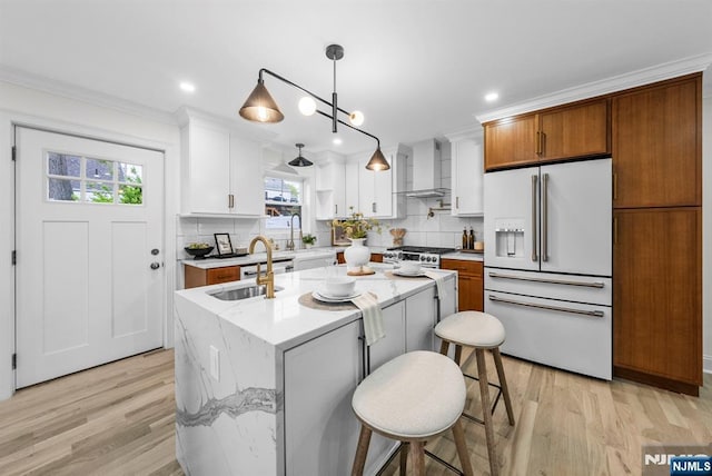 kitchen featuring light wood finished floors, wall chimney range hood, a sink, crown molding, and high quality appliances
