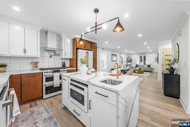 kitchen featuring wall chimney exhaust hood, a sink, built in microwave, freestanding refrigerator, and range with two ovens