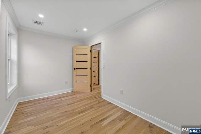 spare room featuring light wood finished floors, baseboards, visible vents, and crown molding