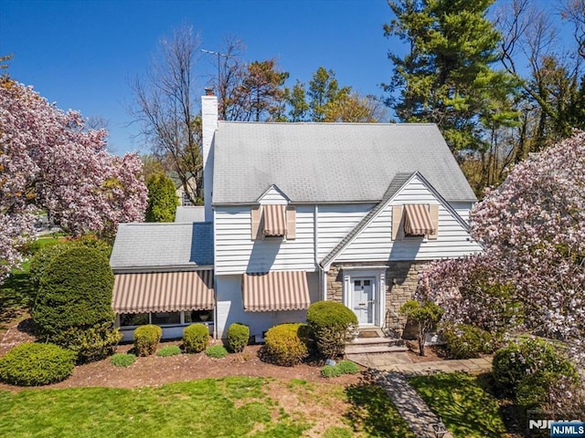 new england style home featuring stone siding, a front lawn, and a chimney