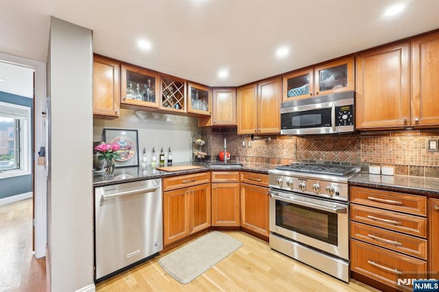 kitchen with light wood-type flooring, backsplash, brown cabinets, and stainless steel appliances