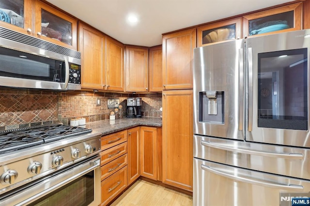 kitchen with dark stone counters, appliances with stainless steel finishes, brown cabinetry, and backsplash