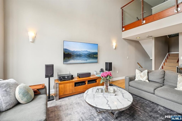 living area with baseboards, stairs, wood finished floors, and a towering ceiling
