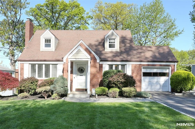 cape cod house featuring a front yard, a chimney, brick siding, an attached garage, and driveway