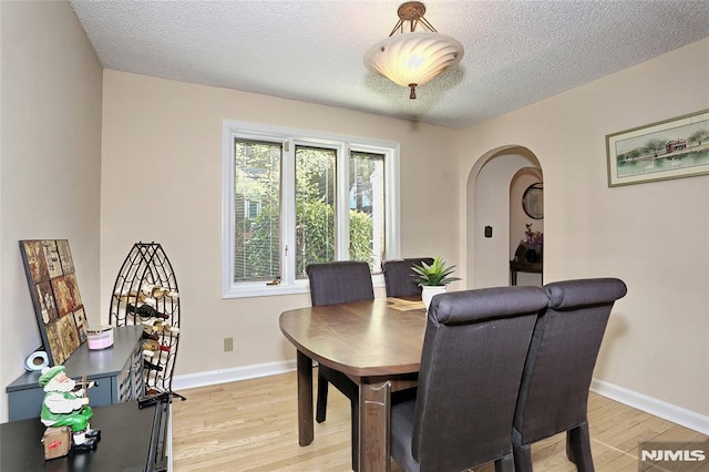 dining area featuring arched walkways, baseboards, a textured ceiling, and light wood-style flooring