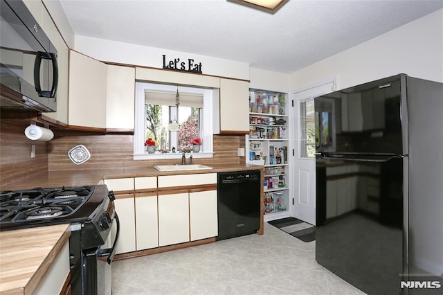 kitchen featuring white cabinets, tasteful backsplash, a sink, light tile patterned floors, and black appliances