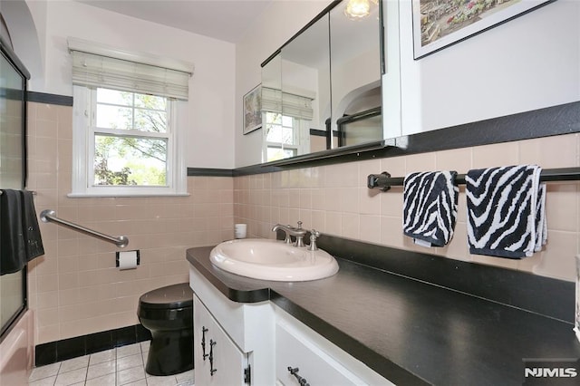 full bath with vanity, toilet, tile patterned floors, a wainscoted wall, and tile walls
