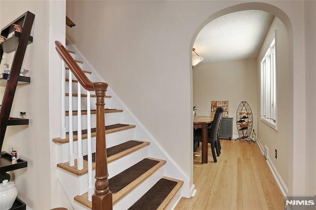 stairs featuring arched walkways, baseboards, a textured ceiling, and wood finished floors