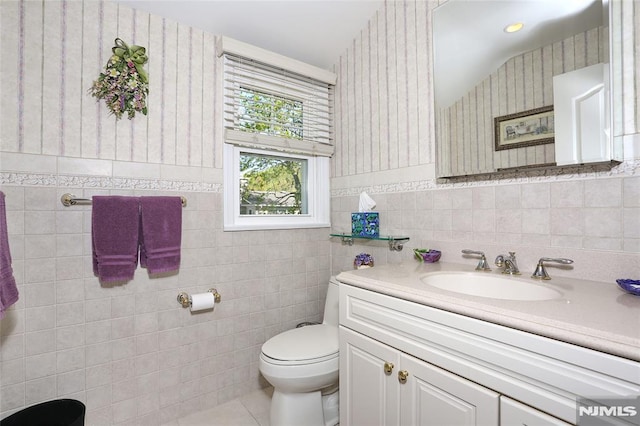 bathroom with vanity, toilet, tile walls, wallpapered walls, and tile patterned floors