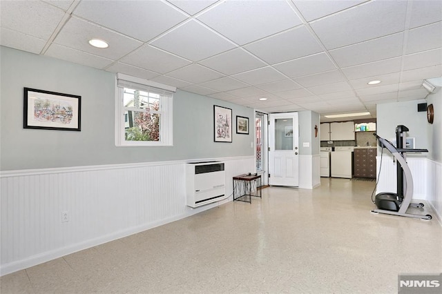 exercise room with heating unit, wainscoting, independent washer and dryer, and a paneled ceiling