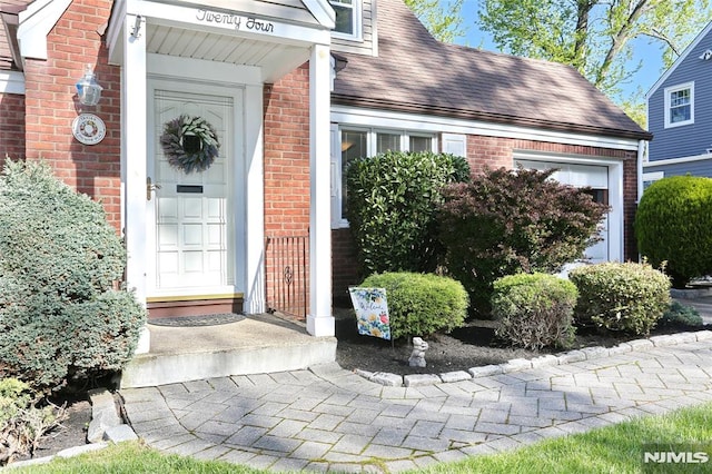 view of exterior entry featuring brick siding and roof with shingles