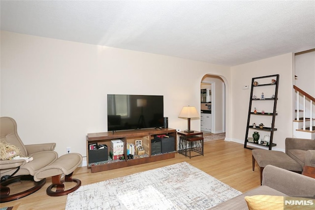 living room with arched walkways, baseboards, stairs, and wood finished floors