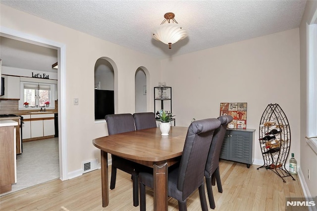 dining room with baseboards, light wood finished floors, a textured ceiling, and visible vents