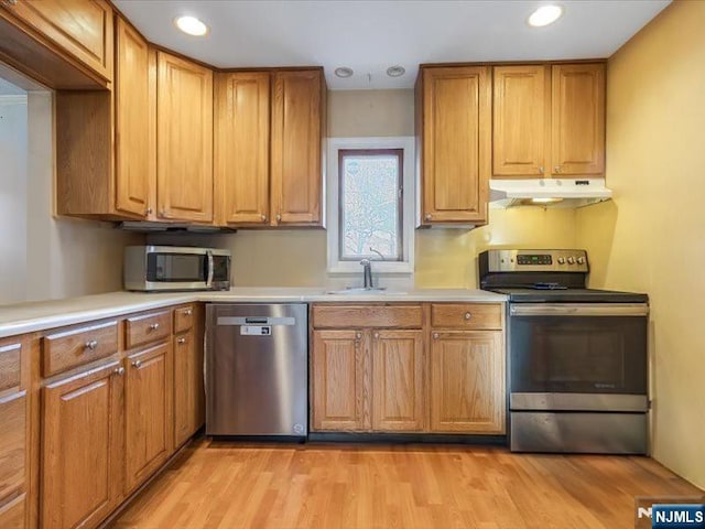 kitchen featuring a sink, brown cabinetry, light wood-style floors, appliances with stainless steel finishes, and under cabinet range hood