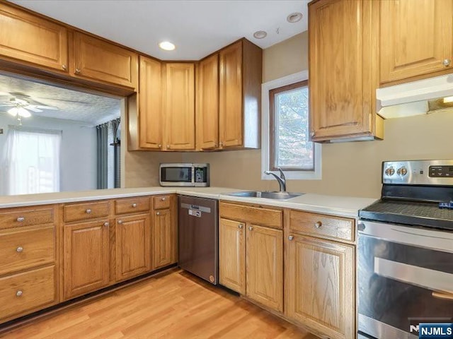 kitchen with light wood finished floors, stainless steel appliances, a sink, light countertops, and under cabinet range hood