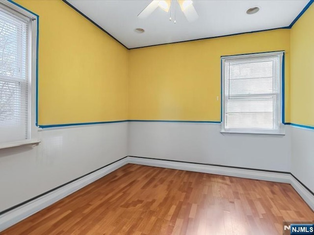 empty room featuring baseboards, a ceiling fan, light wood finished floors, and a healthy amount of sunlight