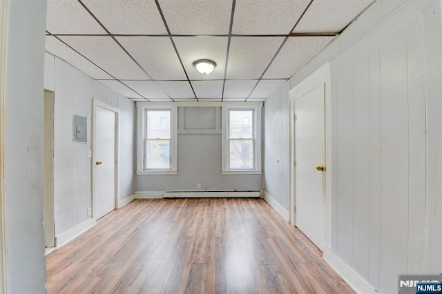 empty room with a baseboard radiator, wood finished floors, a drop ceiling, and baseboards