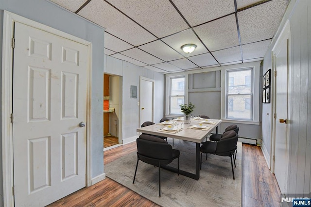dining area with a baseboard radiator, wood finished floors, a drop ceiling, and baseboards