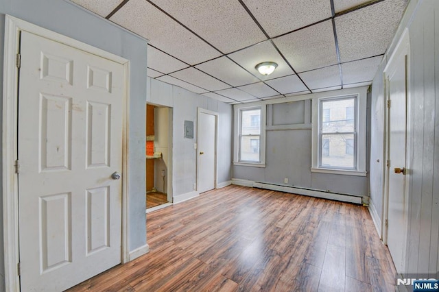 empty room featuring baseboards, a paneled ceiling, baseboard heating, and wood finished floors