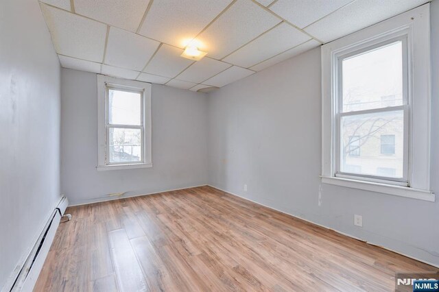 empty room featuring a baseboard radiator, a paneled ceiling, and light wood-style flooring