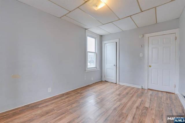 spare room with baseboards, a drop ceiling, and light wood-style flooring