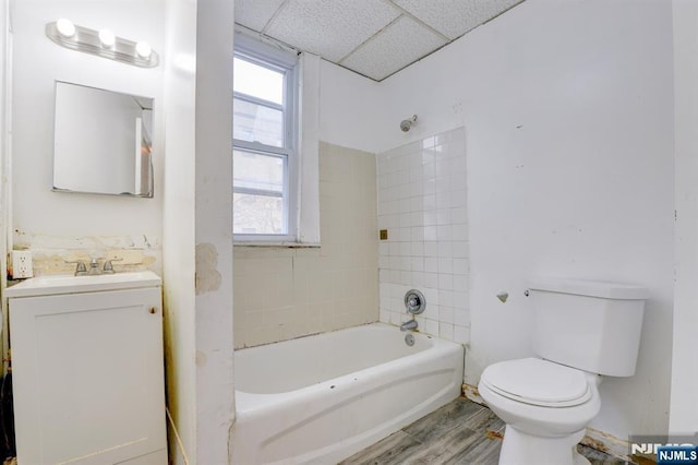 bathroom with a drop ceiling, toilet, wood finished floors, vanity, and shower / tub combination