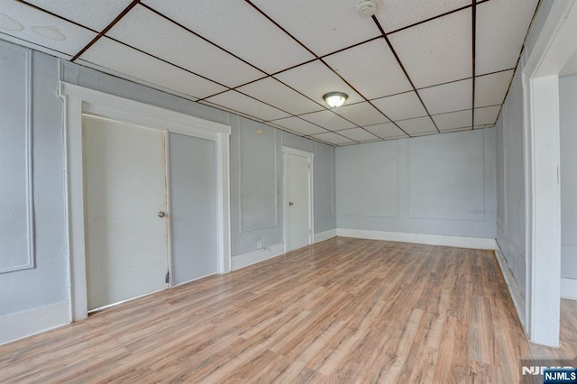 basement with light wood-style floors, a paneled ceiling, and a decorative wall