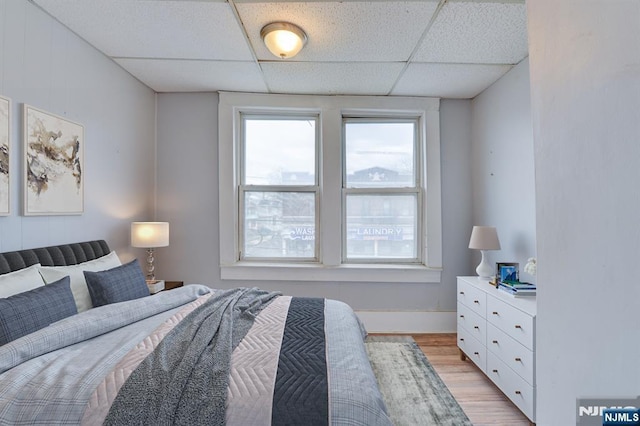 bedroom with light wood-type flooring and a drop ceiling