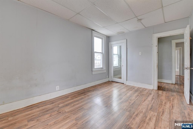 empty room with wood finished floors, a drop ceiling, and baseboards