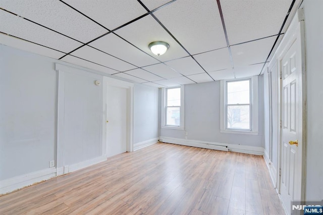 below grade area with a baseboard radiator, baseboards, a drop ceiling, and light wood-type flooring