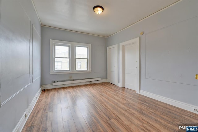 spare room with a baseboard radiator, wood finished floors, and baseboards
