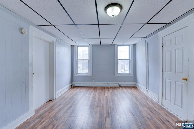 unfurnished bedroom with a baseboard heating unit, baseboards, wood finished floors, and a drop ceiling