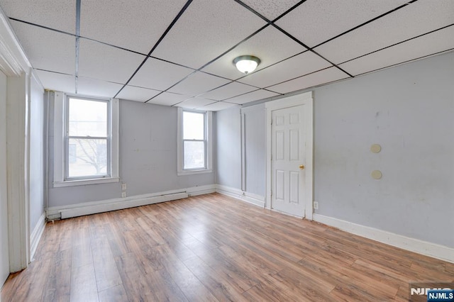 unfurnished room featuring a baseboard heating unit, wood finished floors, baseboards, and a paneled ceiling