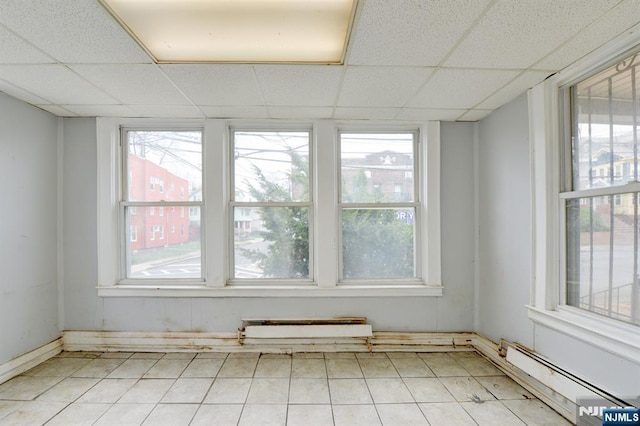 empty room featuring a paneled ceiling, baseboard heating, and light tile patterned floors