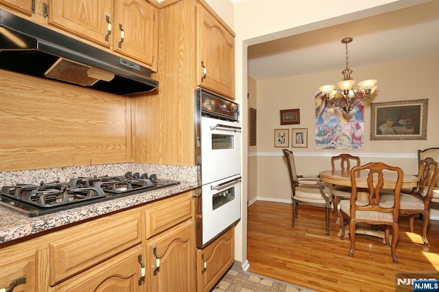 311 Grand Ave Unit 23, Englewood, NJ 07631 - kitchen with under cabinet range hood, black gas stovetop, a notable chandelier, white double oven, and baseboards