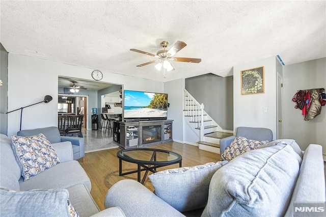 living room featuring a textured ceiling, stairs, a ceiling fan, and wood finished floors