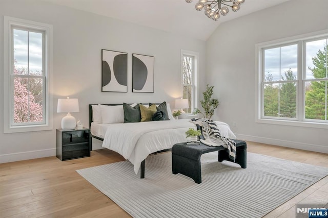 bedroom featuring lofted ceiling, baseboards, light wood finished floors, and a chandelier