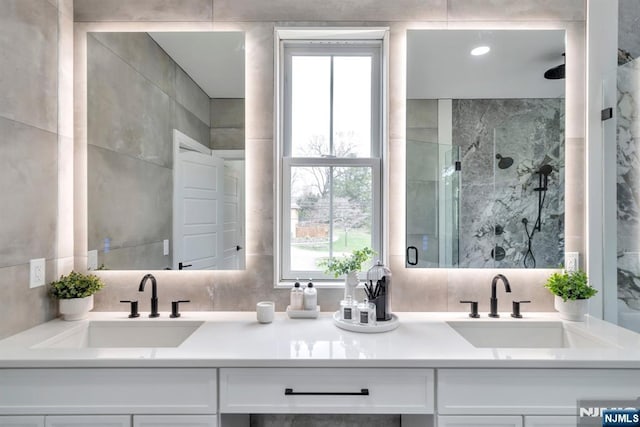 bathroom with a marble finish shower, a sink, and double vanity