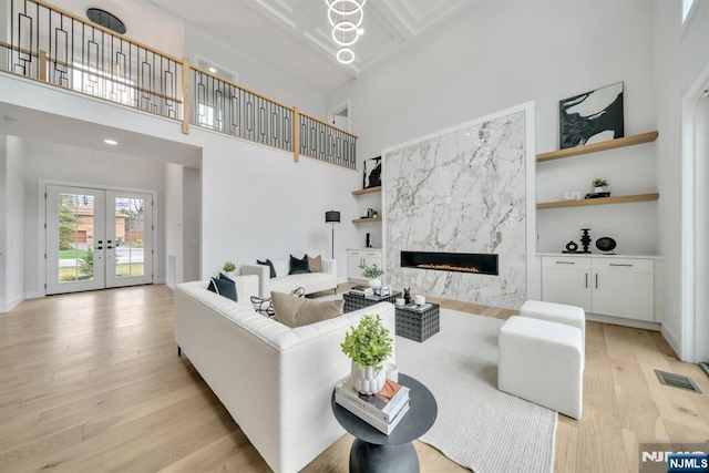 living room with built in shelves, french doors, a towering ceiling, light wood finished floors, and a premium fireplace