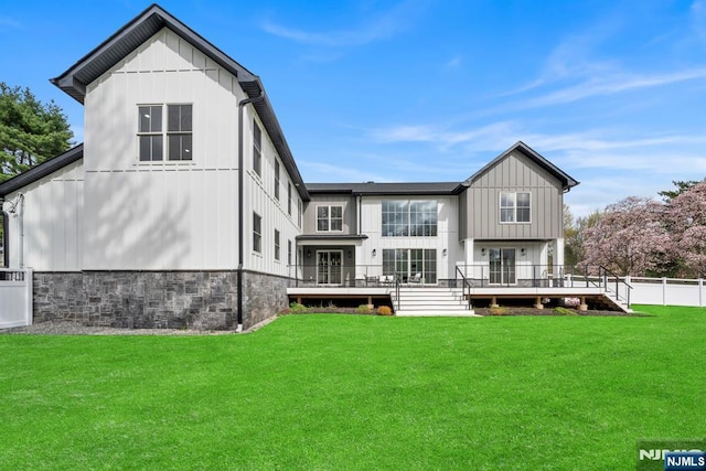 rear view of property featuring fence, a yard, board and batten siding, a wooden deck, and stone siding